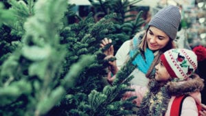 smiling woman and daughter inspecting real christmas trees to make their holiday season more sustainable