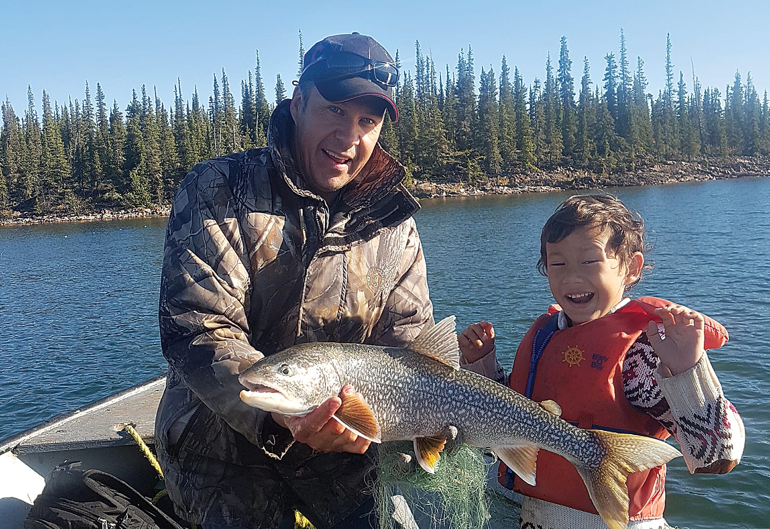 man on boat holding large fish beside excited boy on lake outside Yellowknife