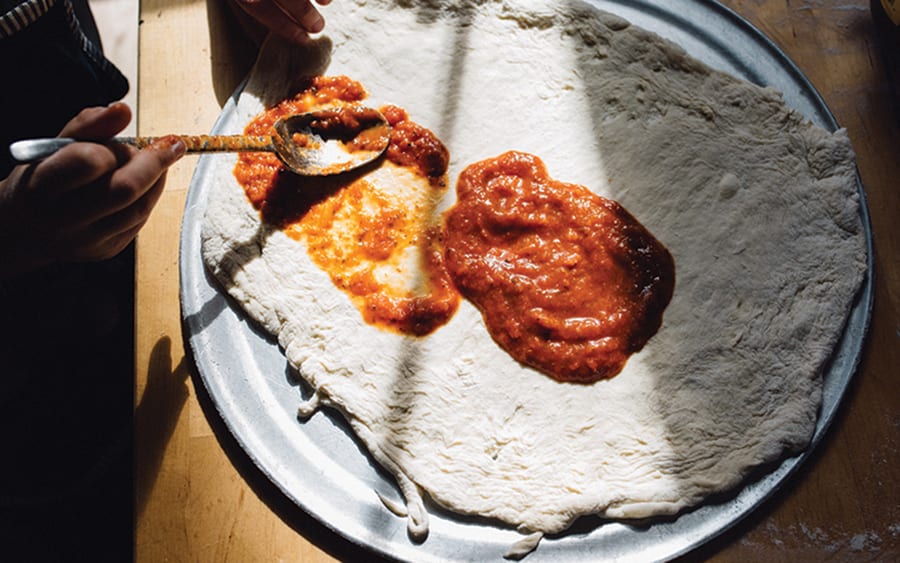 tomato sauce being spread over uncooked pizza dough 
