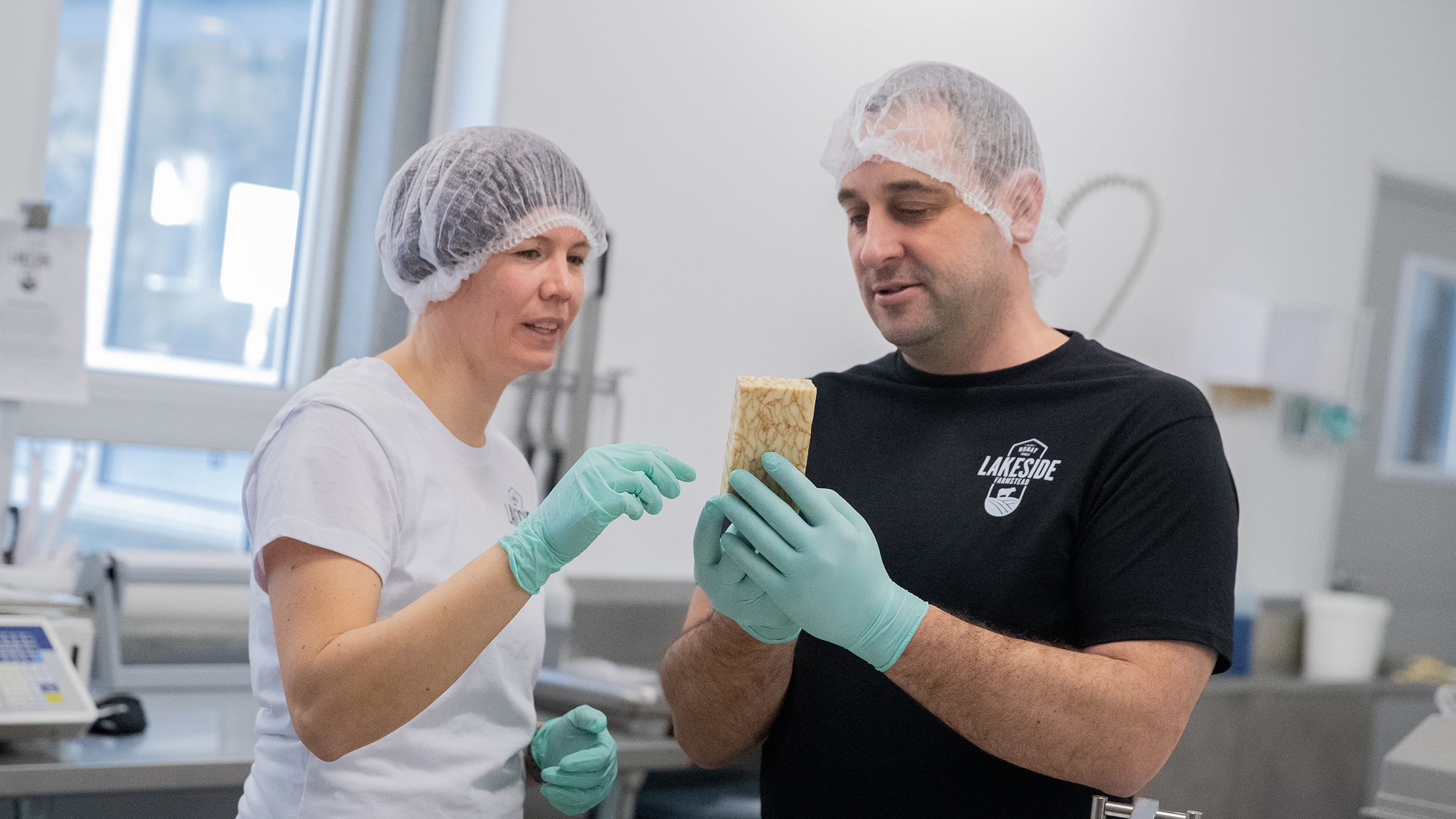 Jeff Nonay standing beside woman wearing hair nets holding block of cheese