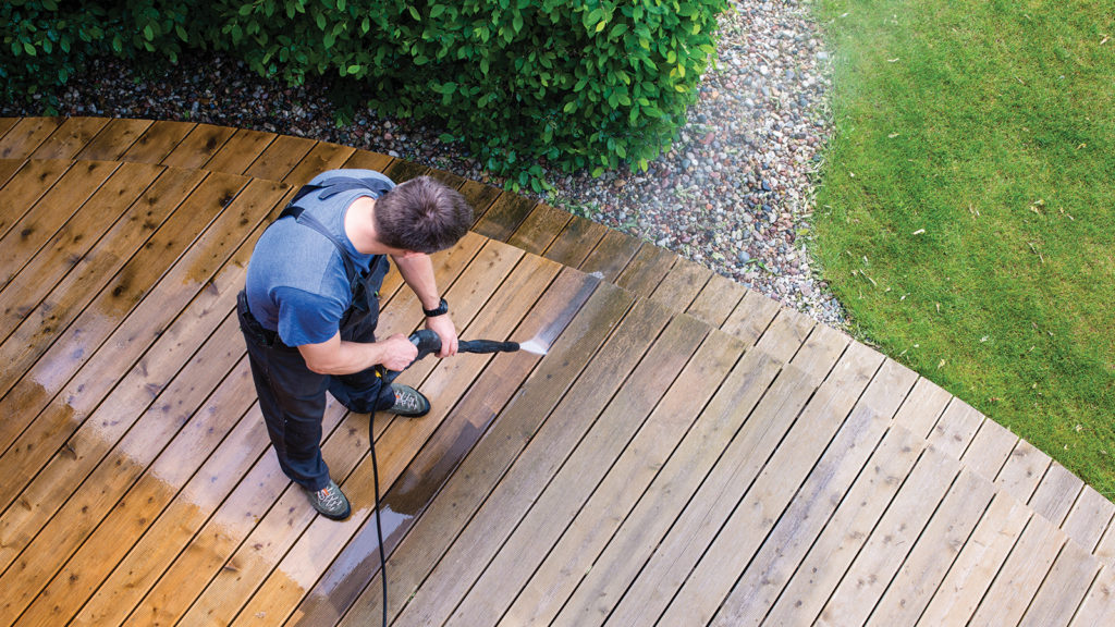 top-down image of man in overalls power-washing wood deck in his dream backyard