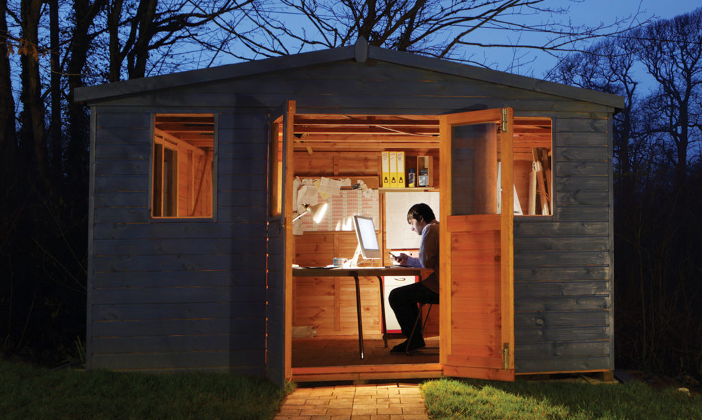 Man using computer inside his dream backyard office shed at dusk