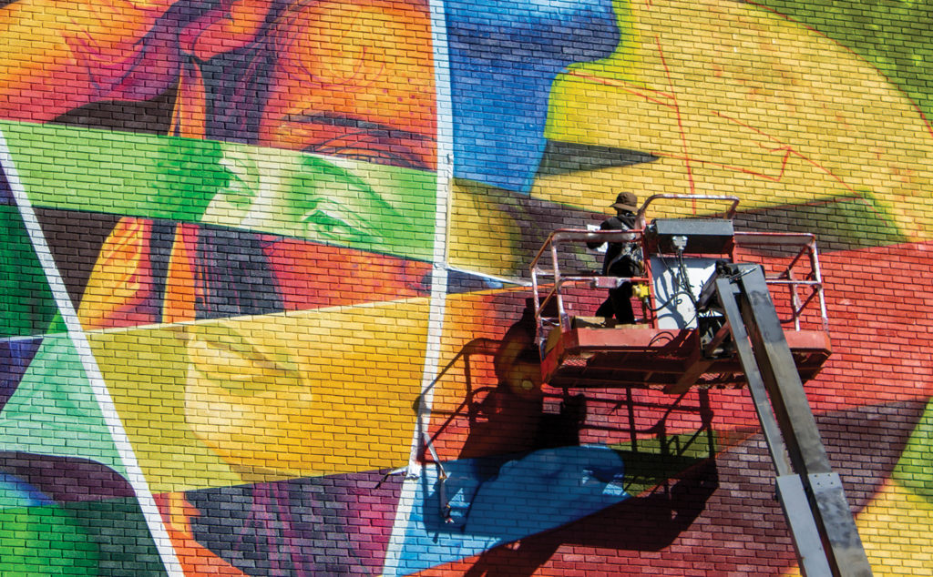 graffiti artist in cherry picker putting finishing touches on colourful mural