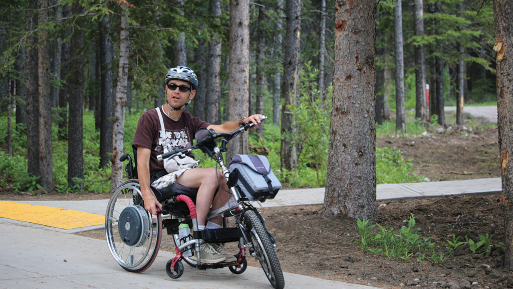 man in adaptive wheelchair on barrier-free trail through coniferous woodland