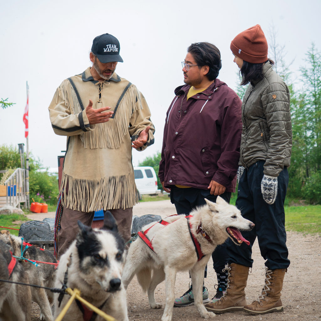 Two men and woman talking while team of sled dogs waits in Churchill Manitoba