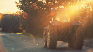 farm vehicle driving on rural road at sunset