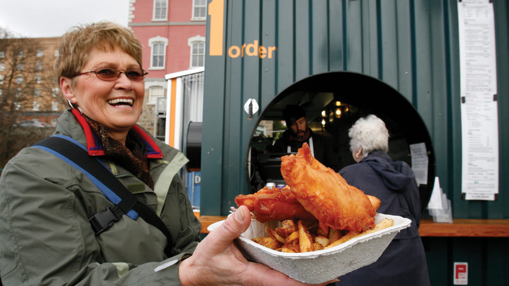 Happy woman holding fish and chips outside of food stall in Victoria
