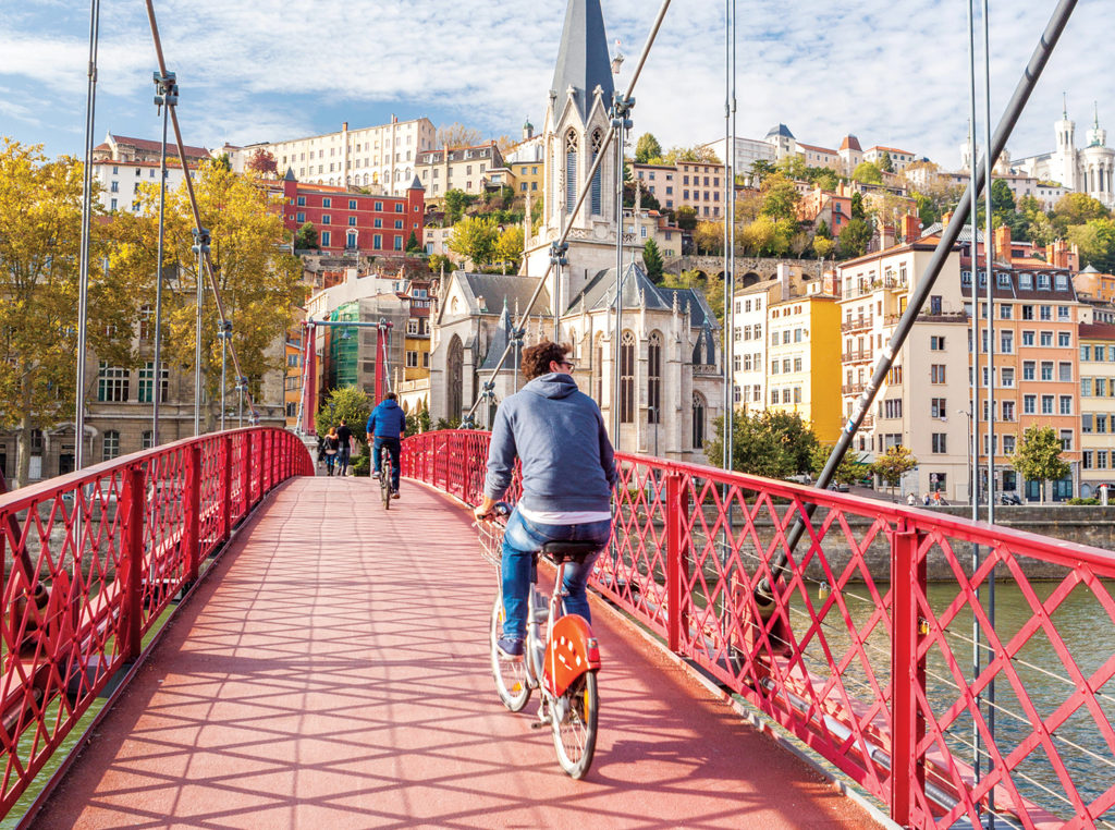Young man cycling over red bridge with church and town in background on an active European holiday