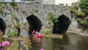 Family in red canoe paddles beneath old stone bridge on an active European holiday