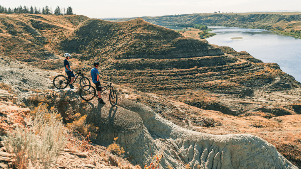 View of rocky, hilly landscape north of Medicine Hat with two mountain bikers looking out over river